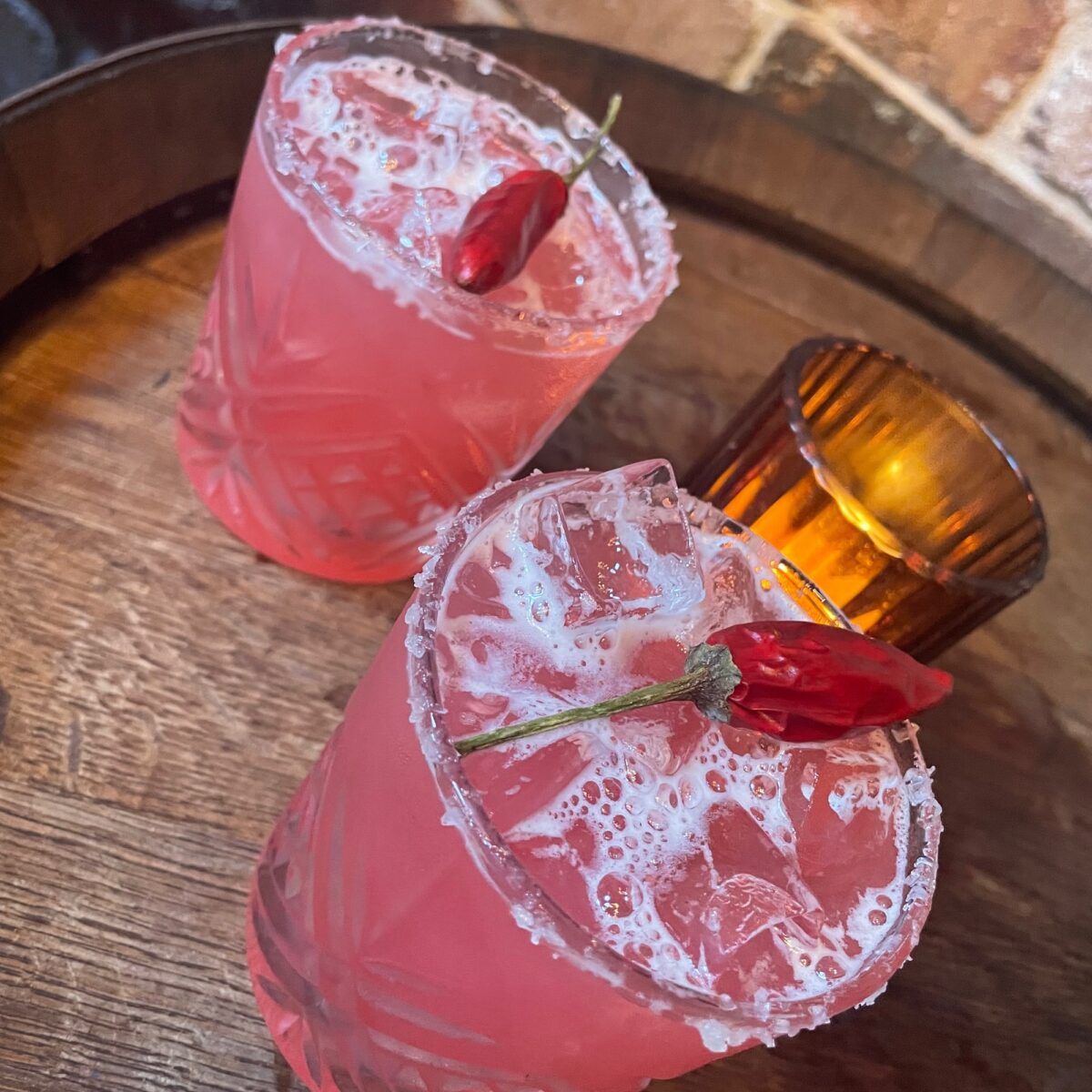 Two glasses with pink liquid and a red chilli pepper on top